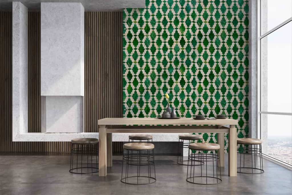 The dining room features a striking green and white geometric patterned wallpaper. The design showcases intricate shapes and lines, delivering a bold contrast with the vertical wooden slats nearby. The green hues range from deep forest tones to lighter shades, while the crisp white provides a clean backdrop, enhancing the dynamic pattern. This wallpaper evokes a modern aesthetic with a touch of Cypriot influence in its geometry.