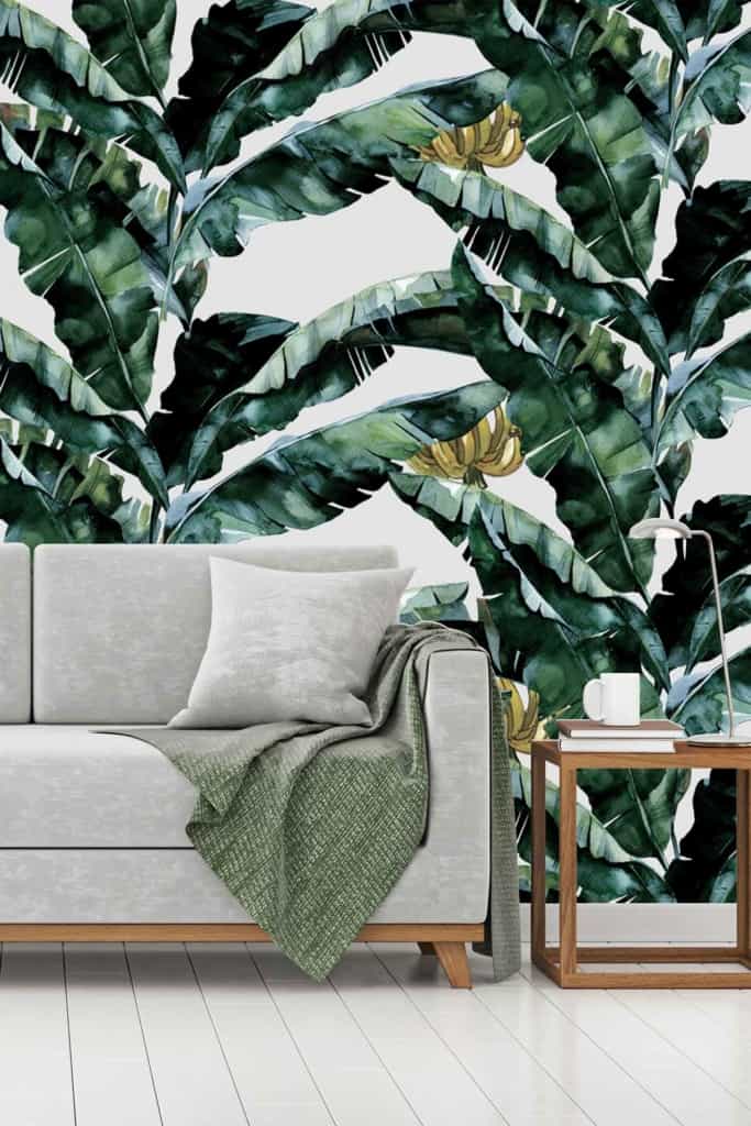 Vibrant tropical leaf wallpaper featuring lush green palm fronds, rich emerald banana leaves, and delicate ferns in various shades of green. Splashes of deep blue and bright yellow accents interspersed throughout for added vibrancy. The background is subtly textured with off-white hues, creating depth and contrast among the leafy elements.