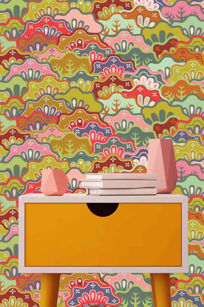 The wallpaper features a vibrant, multicolored abstract pattern with floral and leaf motifs. Elements include various flowers and leaves, creating a nature-inspired design. The primary colors in the pattern are rich greens, bold blues, deep reds, and bright yellows. The overall effect is lively and dynamic with natural elements seamlessly integrated into the abstract art style.