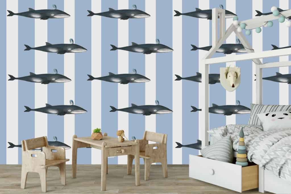 The children's room is adorned with a blue and white striped wallpaper featuring whimsical whale illustrations. The wallpaper's stripes alternate between soothing shades of blue and crisp white, creating a calm yet playful atmosphere. Scattered across the stripes are charming illustrations of gentle whales in various sizes and poses, adding a touch of marine magic to the space. This aquatic-themed wallpaper captures the essence of the sea with its serene color palette and delightful whale motifs, making it perfect for fostering imaginations filled with gentle whale songs.