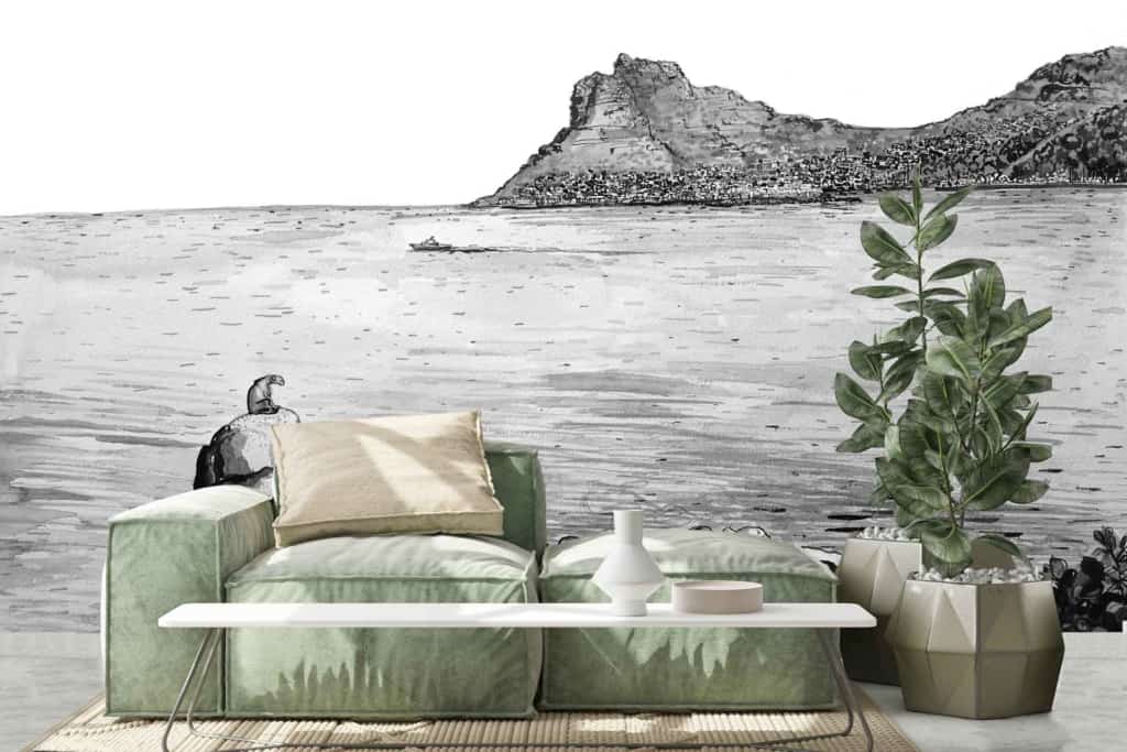 Large mural of Hout Bay coastal scene, featuring Sentinel. Vibrant blues of the ocean, earthy browns and greens of the mountain and cliffs. Tranquil sky with soft white clouds. Serene, natural atmosphere enhanced by vivid nature-inspired hues.