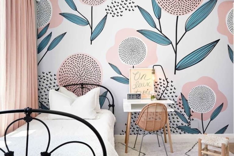 A bedroom with floral-themed wallpaper showcasing large, abstract flowers in pastel colors. The wallpaper features elements such as blossoms, petals, and stems in shades of soft pink, lavender, mint green, and light yellow. It's a dreamy and artistic design full of whimsy and subtle elegance.