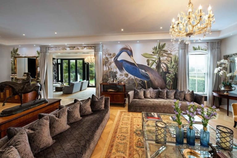 The wall mural features a detailed depiction of a majestic heron, surrounded by an ethereal backdrop of blues and grays. The heron's plumage is intricately rendered in shades of white and soft gray, with hints of gold flecks capturing the light. The surrounding scene includes delicate reeds and water elements, depicted in muted greens and silvery-blue tones. This luxurious wallpaper offers a serene yet striking focal point for any living space.