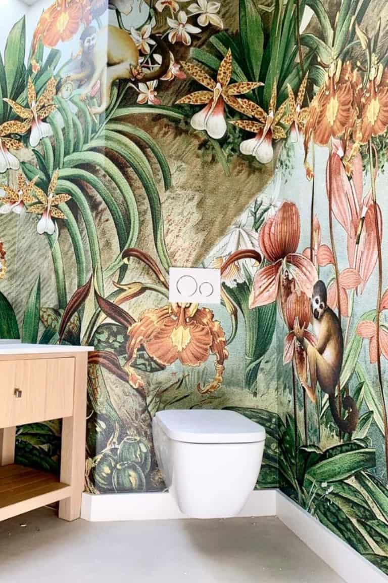 The wallpaper features vibrant jungle-themed elements, including exotic flowers, lush green plants, and playful monkeys. The colors are bright and lively, with a palette that includes bold greens, striking reds, sunny yellows, and rich purples. These elements create an eye-catching and dynamic backdrop perfect for a modern bathroom setting.