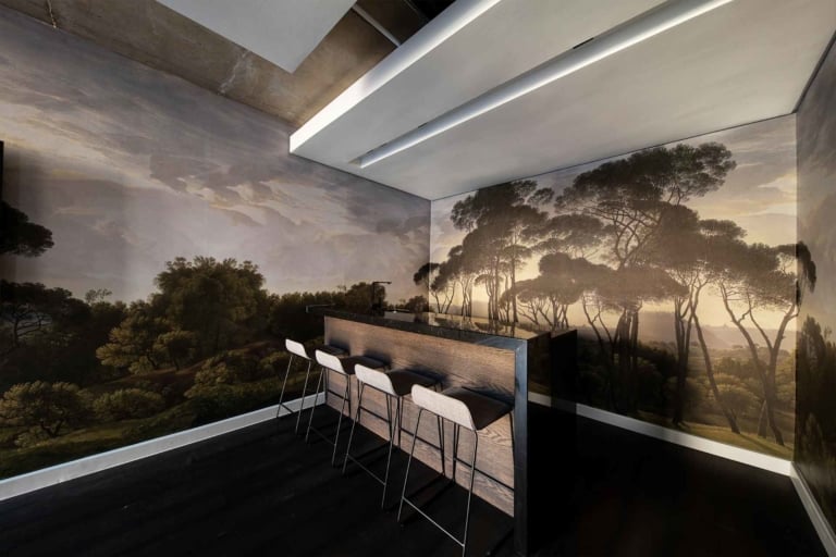 The wallpaper features a serene forest landscape with shades of green, brown, and muted blues. Key elements include towering trees, lush foliage, and gentle streams. Hints of misty white add depth to the scene.