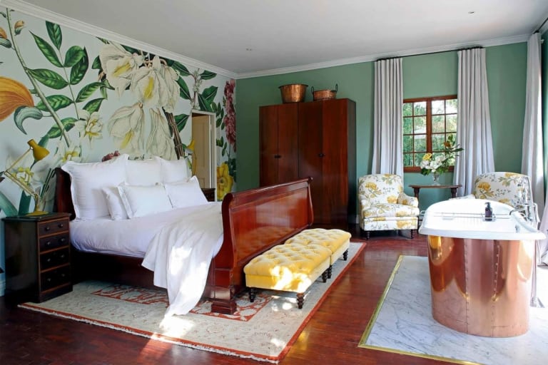 The wallpaper features a vibrant floral pattern with blooms in shades of pink, red, and yellow, complemented by lush green leaves. Delicate vines intertwine throughout the design, adding depth and elegance. This lively and colorful motif creates a stunning backdrop that ties together the room's cheerful and stylish decor.