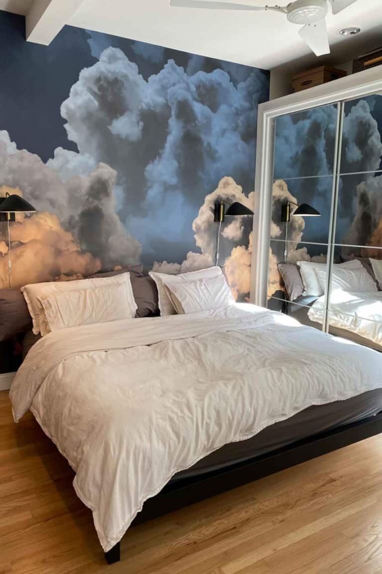 The wallpaper in this modern bedroom features a large mural of a cloudy sky, incorporating soft hues of white, blue, and gray. This serene design adds a calming and ethereal atmosphere to the space. Clouds are delicately detailed against a gradient sky, ranging from light blue at the horizon to deeper blue tones as it ascends.