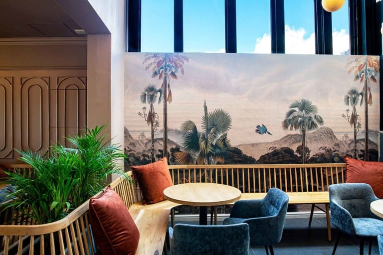 A large mural resembling an artist's portfolio features a scenic landscape with palm trees and a flying bird. The wallpaper includes elements of nature, primarily consisting of green palm trees and the blue sky, with the bird possibly showcasing various shades for realism. Natural light enhances the vivid colors on the wall.