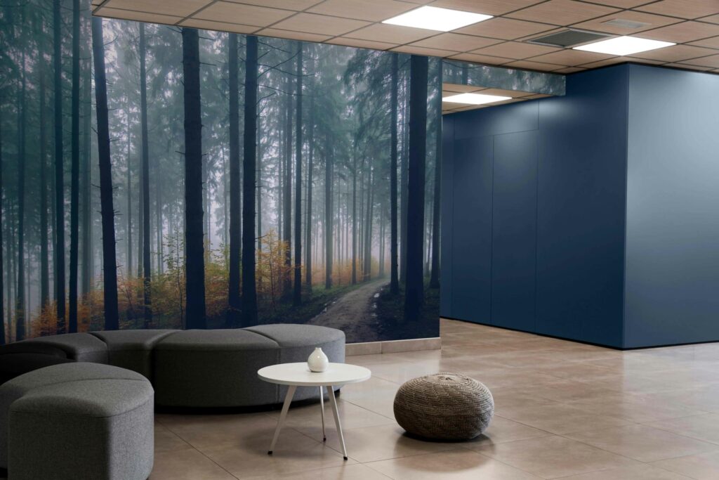 The wallpaper in the modern lobby features a forest theme with towering trees, their leaves forming a lush canopy overhead. The path to freedom meanders through the dense green foliage, leading the eye toward a bright clearing in the distance, symbolizing openness and possibility. The palette incorporates various shades of green from deep emerald to light moss, mixed with earthy browns for tree trunks and rich soil. Delicate highlights of sunlight filter through the branches, adding glimmers of gold that evoke early morning or late afternoon rays in this serene woodland scene.