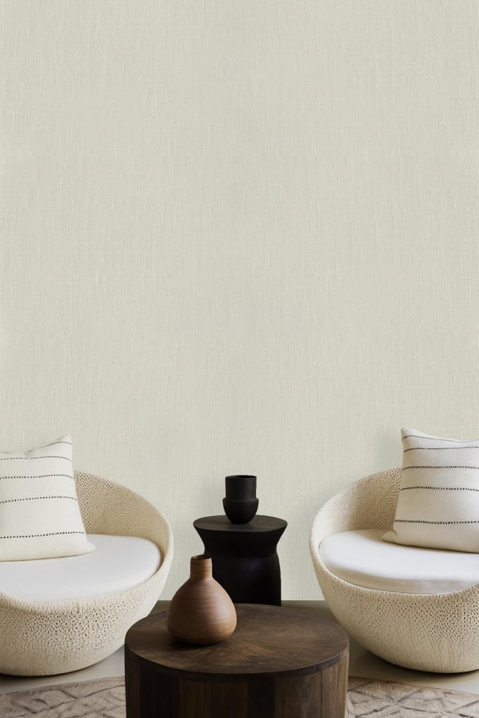 The wallpaper features a plain off-white color, serving as a minimalist backdrop that complements the modern living space. The neutral hue creates a serene atmosphere, allowing the room's furnishings to stand out. No intricate patterns or bold designs adorn this wallpaper; its simplicity enhances the elegance of the cushioned chairs, coffee table, and ceramic vases placed in the setting.