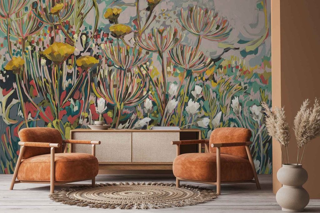 Vibrant floral wallpaper featuring abstract wildflowers, with prominent sewejaartjies and wilde fennel motifs. Color palette includes bold pinks, yellows, greens, and soft pastels on a neutral or muted background. Large-scale botanical elements and expressive brushstrokes create an artistic mural effect.
