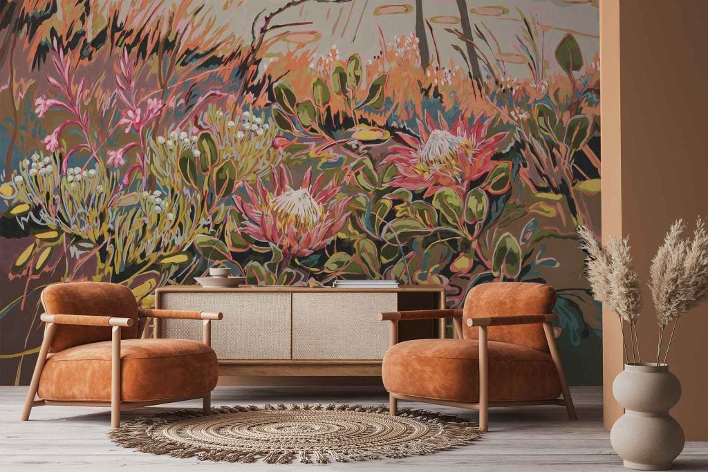 Colorful floral wallpaper featuring large pink King Protea and Watsonia flowers, with green foliage and vibrant botanical elements. The mural has bold, artistic flower designs in shades of pink, white, green, and touches of yellow.