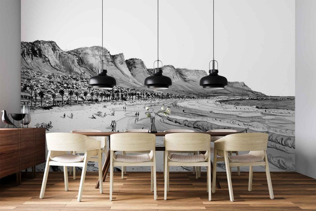 The wallpaper is a large black-and-white mural featuring a beach scene. Elements include detailed mountains in the background, rolling ocean waves, sandy shorelines, and groups of small figures representing people enjoying the beach. The imagery uses only shades of black, white, and gray for a high-contrast, photographic look.