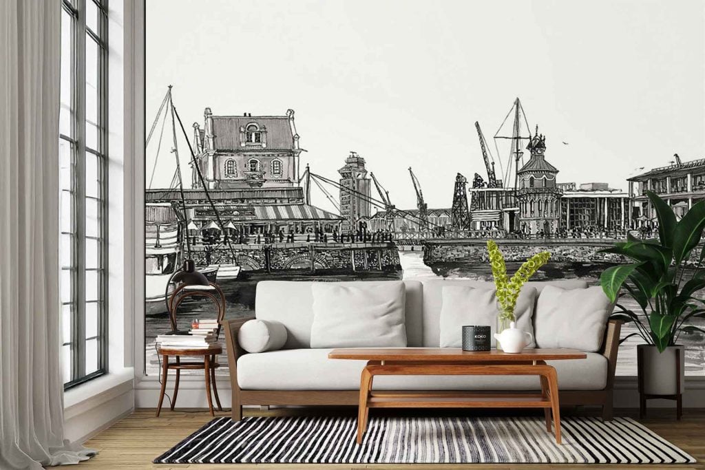 The wallpaper features a striking black-and-white cityscape of Muizenberg, showcasing detailed buildings, boats docked at the waterfront, tall cranes in the background, and a solitary swimmer in the water. The design uses strong contrasts between deep blacks, crisp whites, and subtle grays to emphasize architectural lines and reflections on the water. Key elements: buildings, boats, cranes, lone swimmer; monochrome color palette; cityscape; waterfront scene.