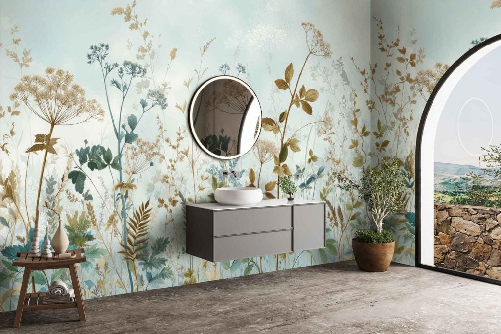 Botanical wallpaper featuring lush green leaves, delicate ferns, and subtle eucalyptus branches intertwined with muted pastel flowers. The color palette includes deep forest green, sage, soft blush pinks, creamy whites, and hints of golden yellow. Patterns are layered for a natural, organic texture with occasional touches of watercolor blue mimicking mountain mist.