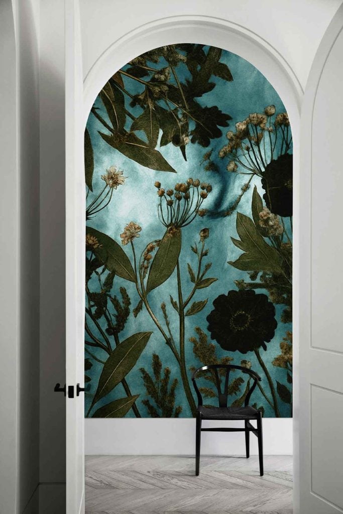 Teal and black floral wallpaper with Meadowlands-inspired patterns covers a large arched wall, adding dramatic contrast to the white walls and herringbone-patterned floor.