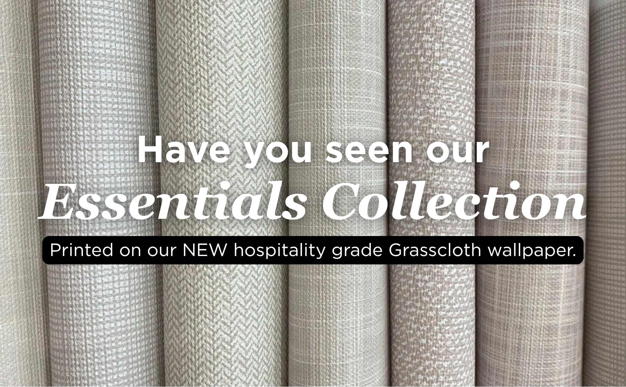 Rolled neutral-toned wallpaper samples displayed vertically, featuring textured grasscloth patterns in beige, cream, and taupe shades. Subtle woven elements highlight the natural look of the hospitality grade collection.