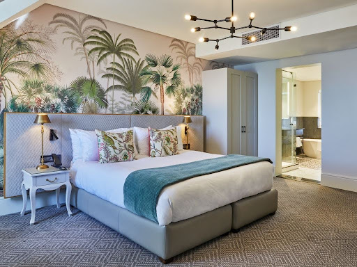 Tropical-themed wallpaper featuring bold green palm leaves, vibrant foliage patterns, and colorful botanical elements creates a lush, exotic backdrop in the hotel room.