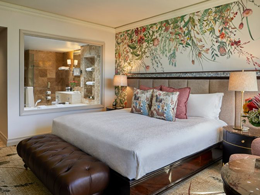 Floral accent wall with intricate flower patterns in soft pinks, greens, and blues stands out as the main feature, adding vibrant color and lively design to the hotel room decor.