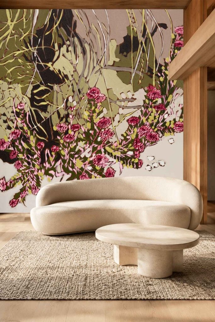 A large, colorful, abstract floral mural dominates the background, featuring prominent green, pink, and beige tones with bold shapes and layered elements. The wallpaper stands out as a vibrant centerpiece in the room.