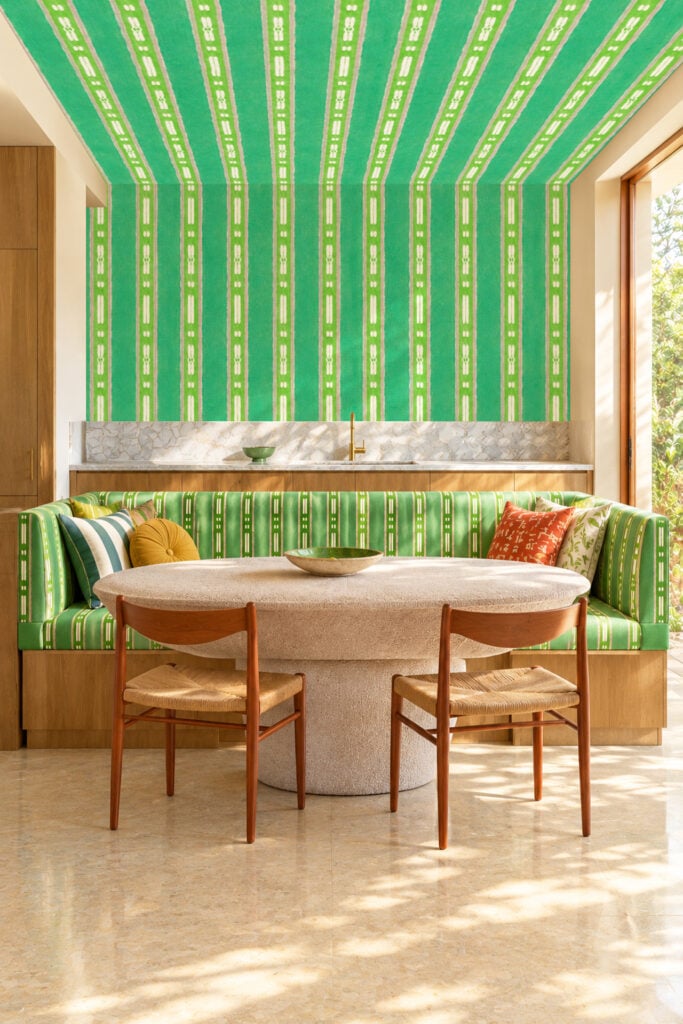 Green striped wallpaper covers the wall and ceiling above the bench, creating a cohesive pattern of alternating light and dark green stripes that adds a bold, modern touch to the dining area.
